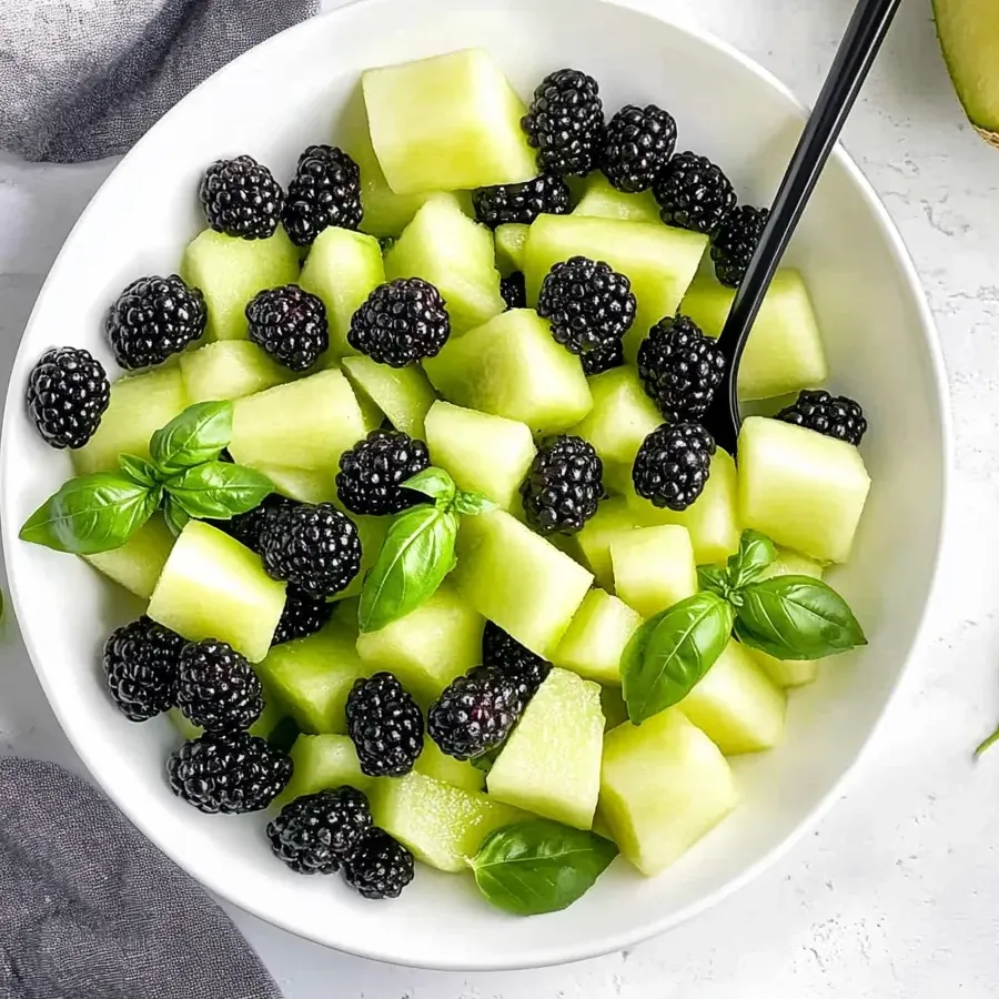 A bowl of fruit salad with blackberries, honeydew, and basil.