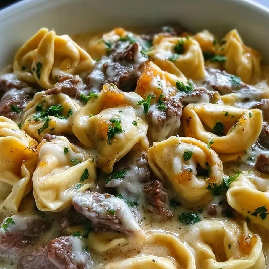 A bowl of cheesesteak tortellini in creamy provolone sauce.