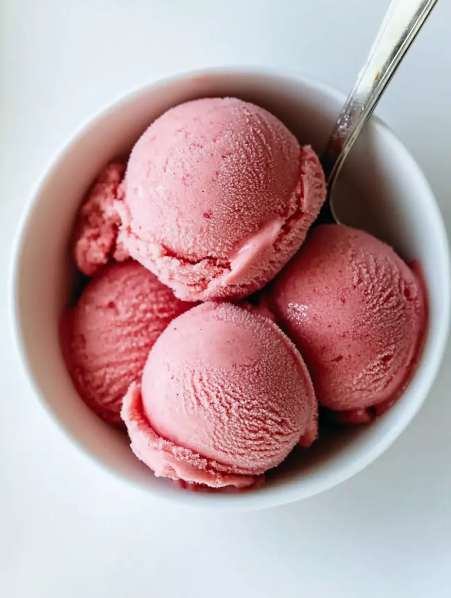 A bowl of pink frozen yogurt with a spoon in it.