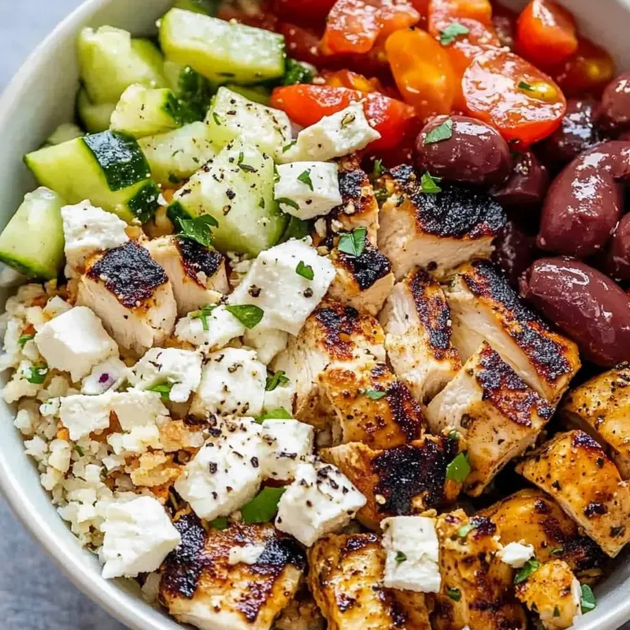 A bowl of food with chicken, tomatoes, cucumbers, and olives.