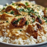 A bowl of rice and chicken covered in a creamy sauce.