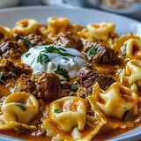 A steaming plate of cheesy pasta mixed with beef in enchilada sauce.