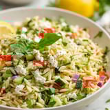 A bowl of rice with vegetables and feta cheese.