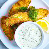 A white plate with a bowl of tartar sauce and some breaded fish.