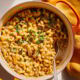 A bowl of macaroni and cheese with meat and vegetables.
