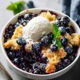 A bowl of blueberries with a scoop of ice cream on top.