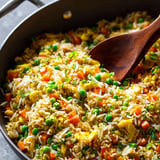 A wooden spoon in a pan of rice and vegetables.