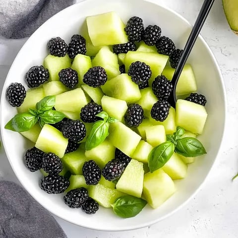 A bowl of fruit salad with blackberries, honeydew, and basil.