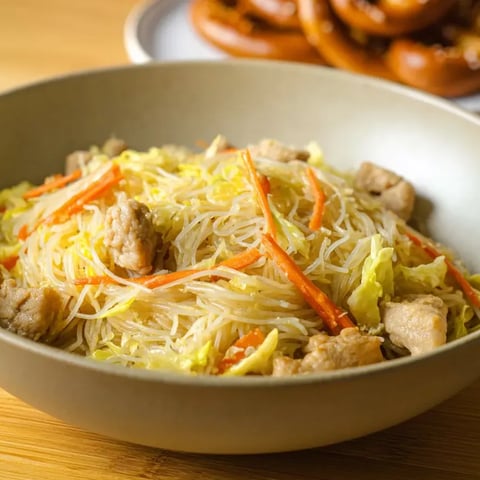 A bowl of pancit with meat and vegetables.
