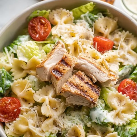 A bowl of pasta salad with chicken and tomatoes.